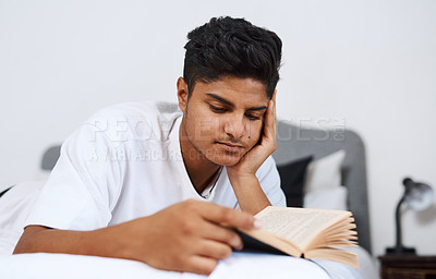 Buy stock photo Cropped shot of a young man reading a book while lying on his bed