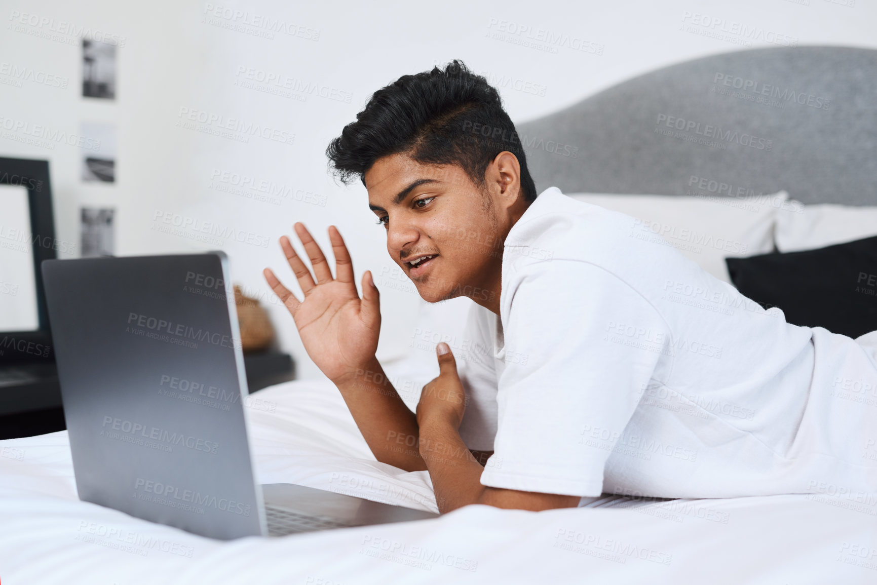 Buy stock photo Cropped shot of an young man using his laptop while lying on his bed