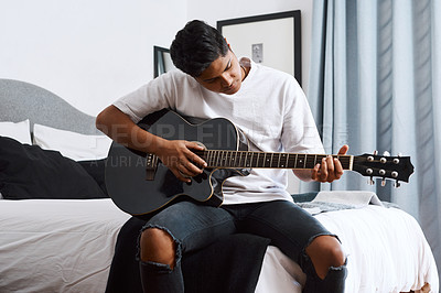 Buy stock photo Shot of a young man playing the guitar while sitting at home