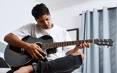 Buy stock photo Shot of a young man playing the guitar while sitting at home