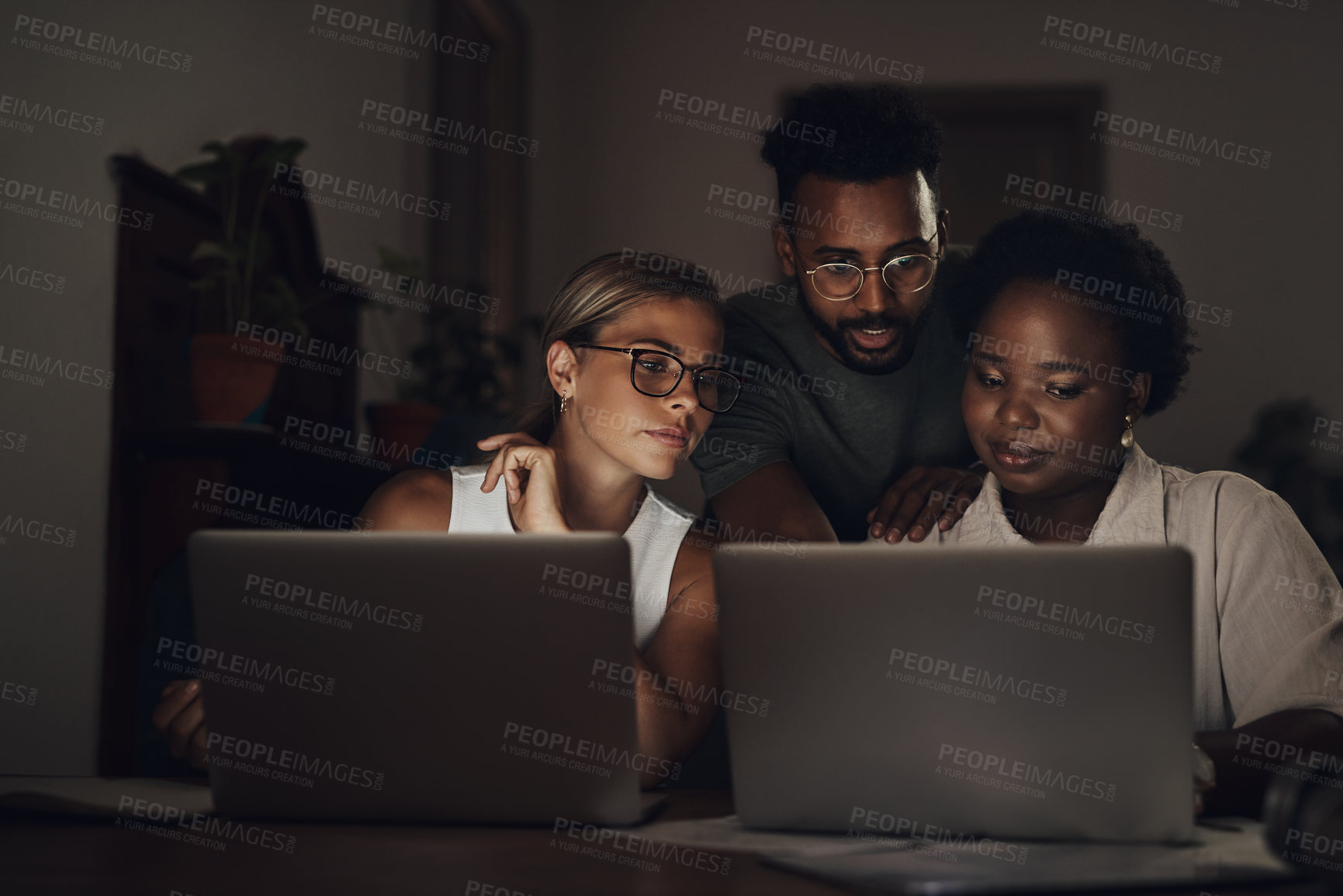 Buy stock photo Shot of a group of young businesspeople using two laptops during a late night at work