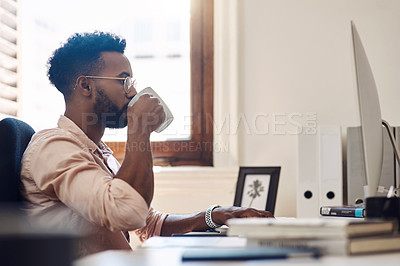 Buy stock photo Shot of a young businessman drinking coffee while working on a computer in an office