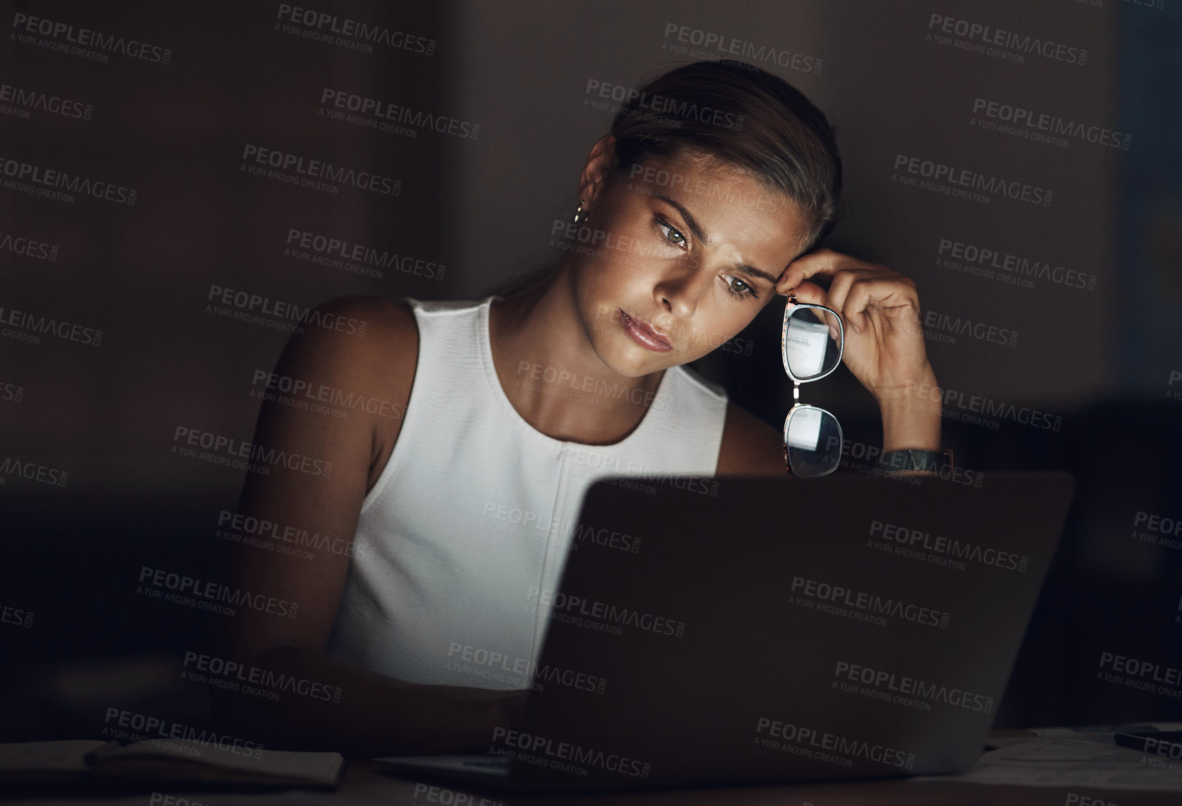 Buy stock photo Shot of a young businesswoman looking worn out while using a laptop during a late night at work