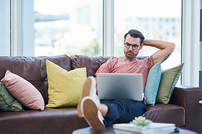 Buy stock photo Shot of a young man using a laptop while relaxing on a sofa