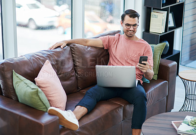 Buy stock photo Shot of a young man using a laptop and smartphone while relaxing on a sofa