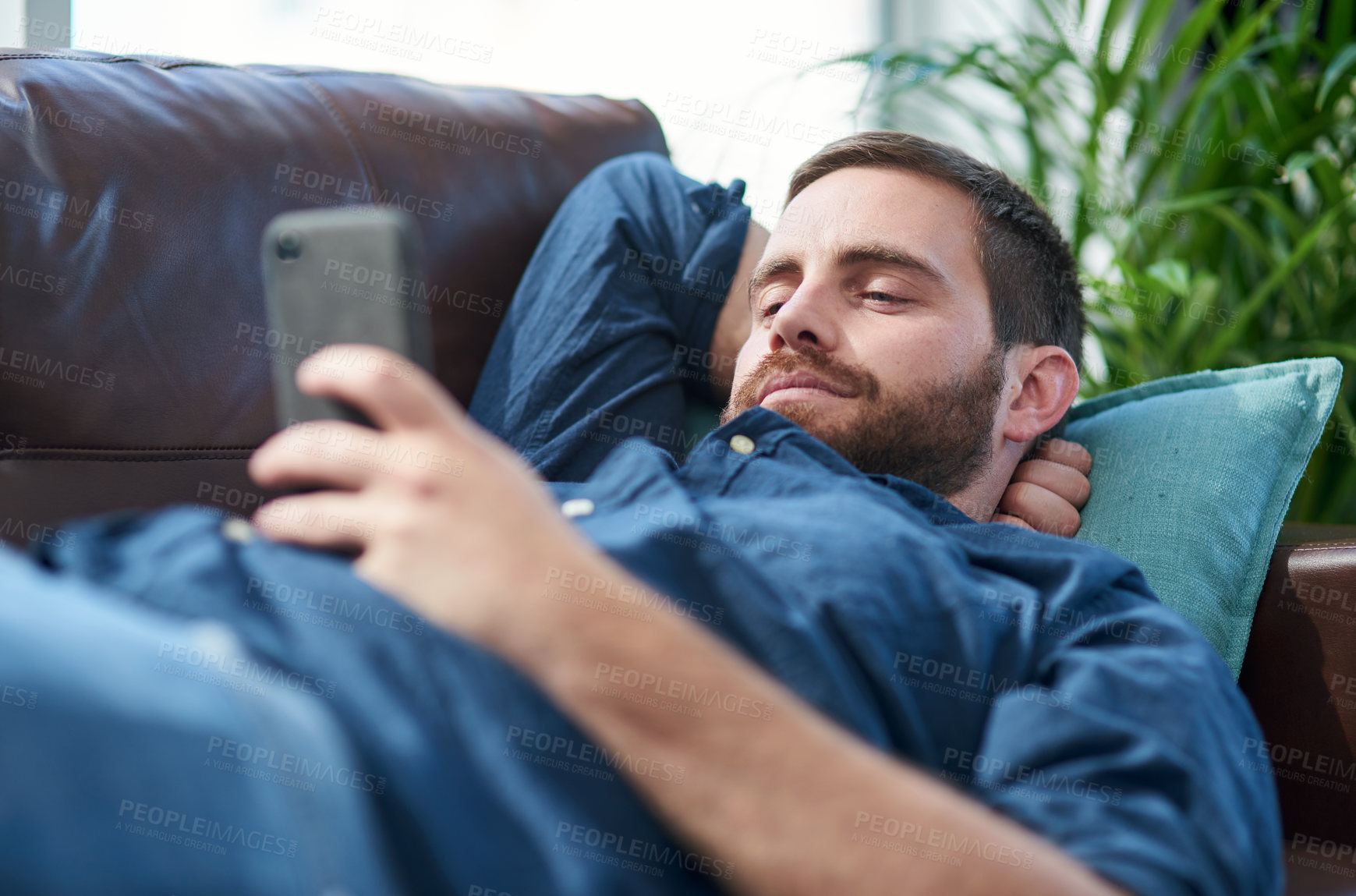 Buy stock photo Shot of a young man using a smartphone while relaxing on a sofa
