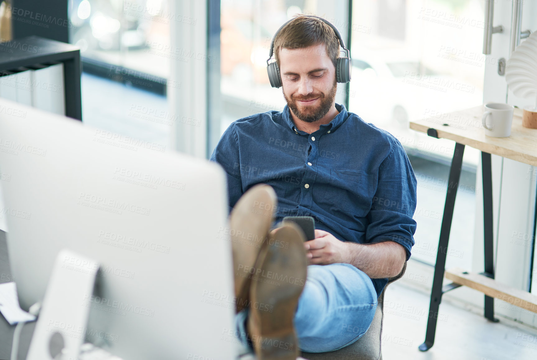 Buy stock photo Headphones, cellphone and businessman in office with relax listening to music, radio or podcast online. Happy, audio tech and male designer streaming song, playlist or album on internet in workplace.