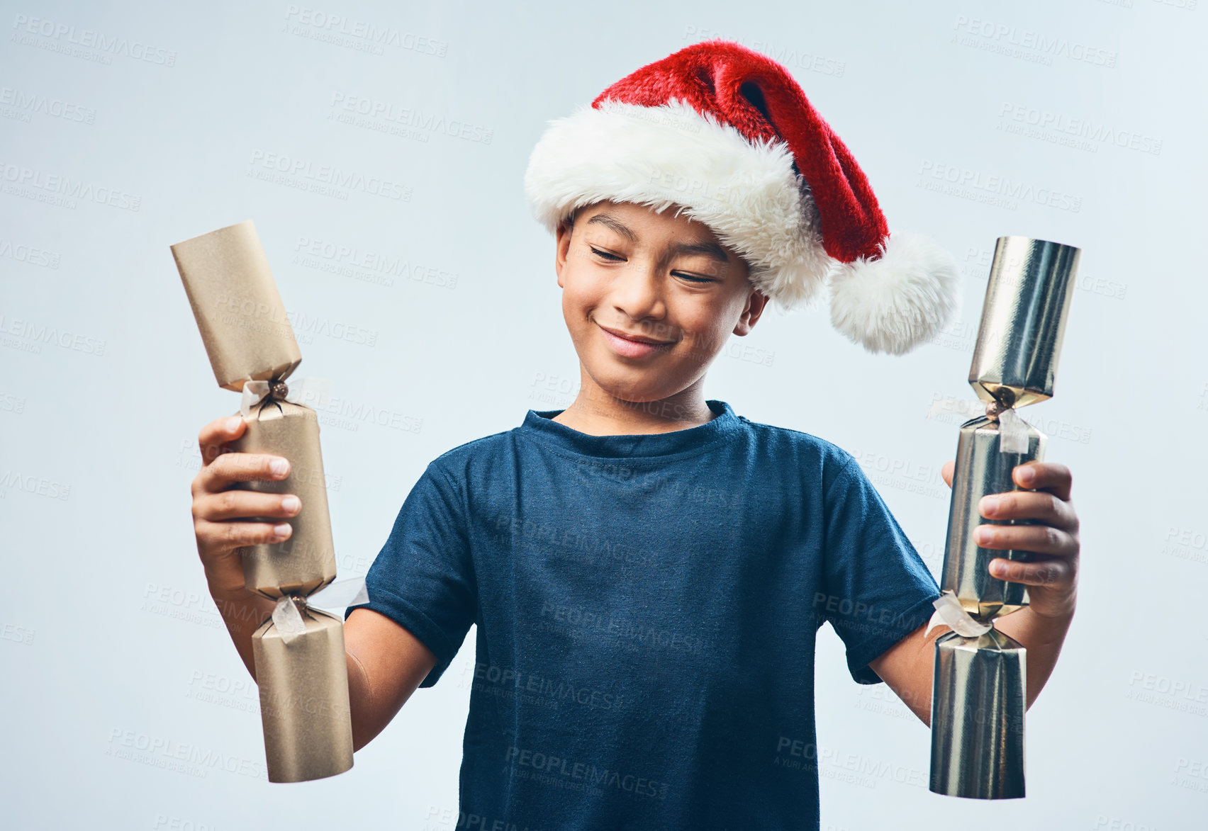 Buy stock photo Studio shot of a cute little boy wearing a Santa hat and holding two Christmas crackers against a grey background