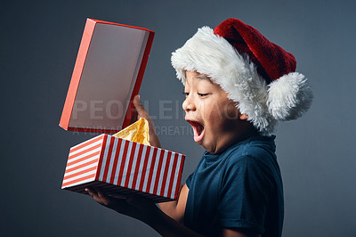 Buy stock photo Studio shot of a cute little boy opening a Christmas present against a grey background
