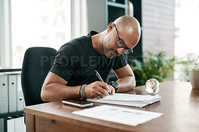 Buy stock photo Shot of a mature businessman filling out paperwork at his desk in a modern office