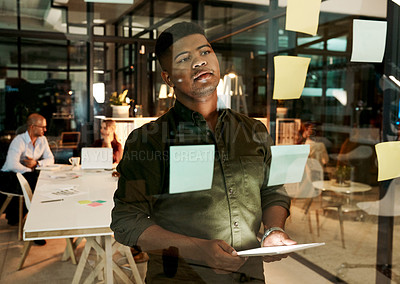 Buy stock photo Shot of a young businessman using a digital tablet during a late night brainstorming session in a modern office