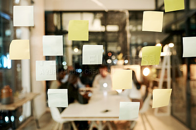 Buy stock photo Shot of sticky notes on a glass window with businesspeople having a late night brainstorming session in a modern office