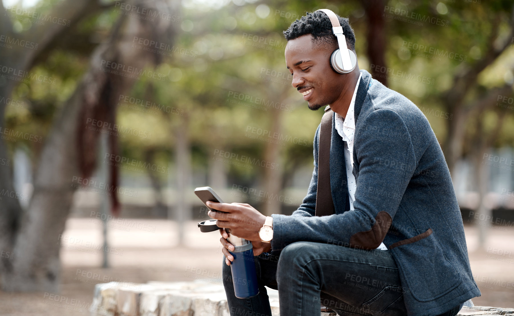 Buy stock photo Businessman browsing social media on his phone and enjoying his music playlist app in headphones outdoors. Young, happy and casual african male relaxing in a nature park outside during a break 