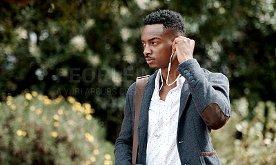 Buy stock photo A stylish, trendy and serious young man going to work while listening to music using earphones. A young African American male entrepreneur walking outdoors with nice style or fashion