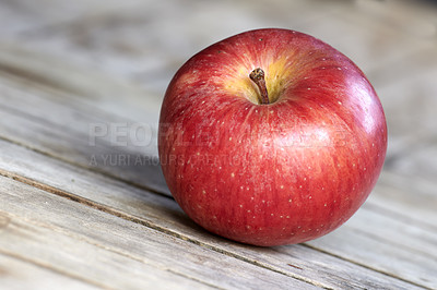 Buy stock photo Single red apple on a wooden table indoors. Eat healthy and watch your diet. Fruit contains essential vitamins to boost your immunity. Closeup of a delicious snack vegans and vegetarians can enjoy