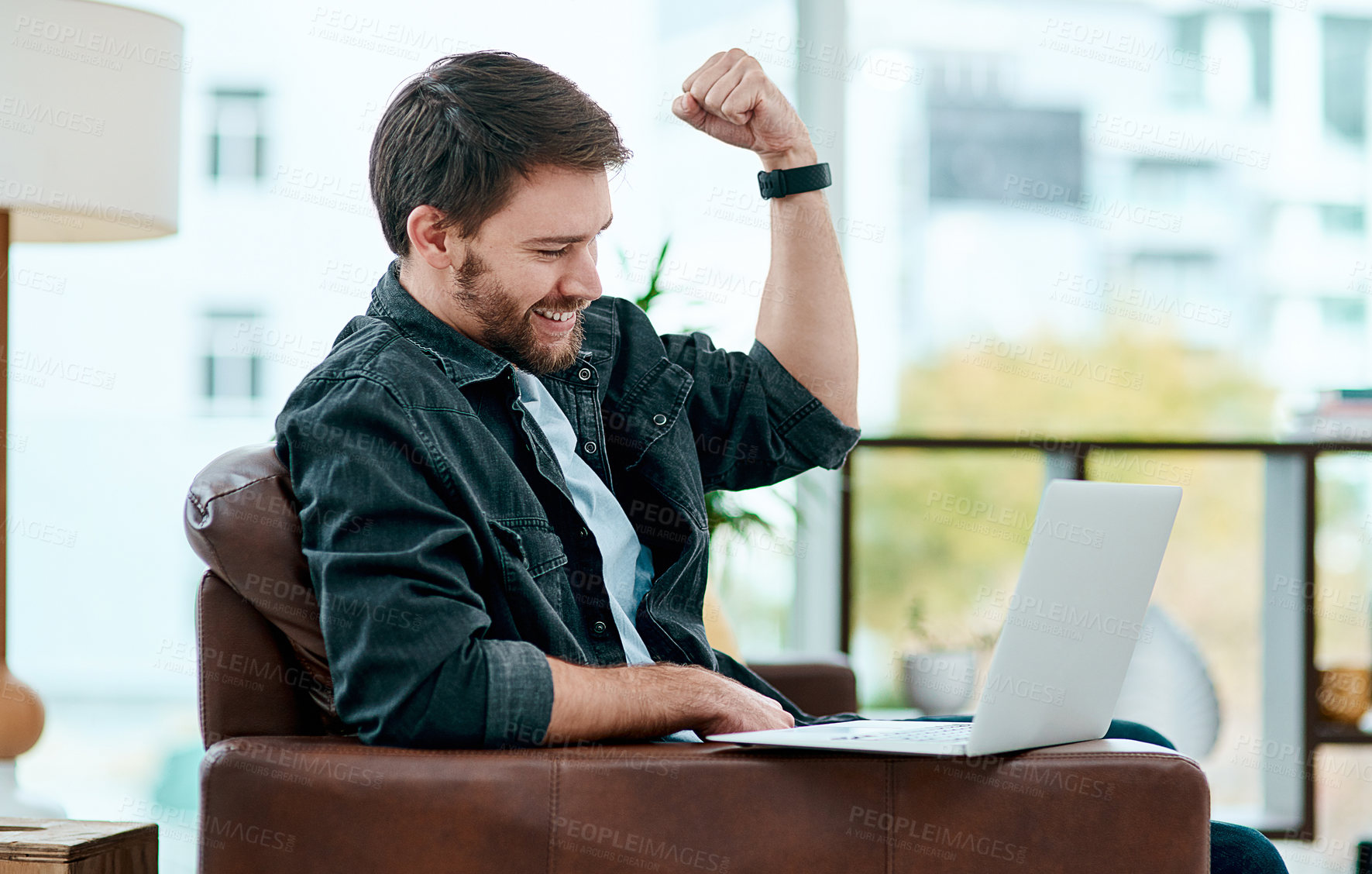 Buy stock photo Shot of a young man using a laptop on the sofa at home and cheering