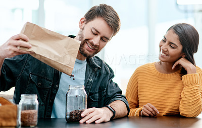 Buy stock photo Coffee, jar and sorting with interracial couple in kitchen of home together to organize beans or groceries. Glass, paper bag or pouring with man and woman in apartment for beverage or caffeine