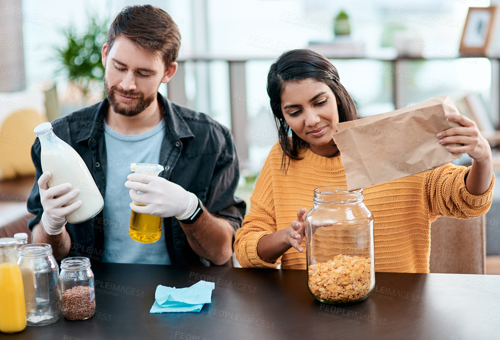 Buy stock photo Cereal, jar and sanitizing with interracial couple in kitchen of home together to organize food or groceries. Cleaning, glass or paper bag with man and woman in apartment for diet, health or wellness