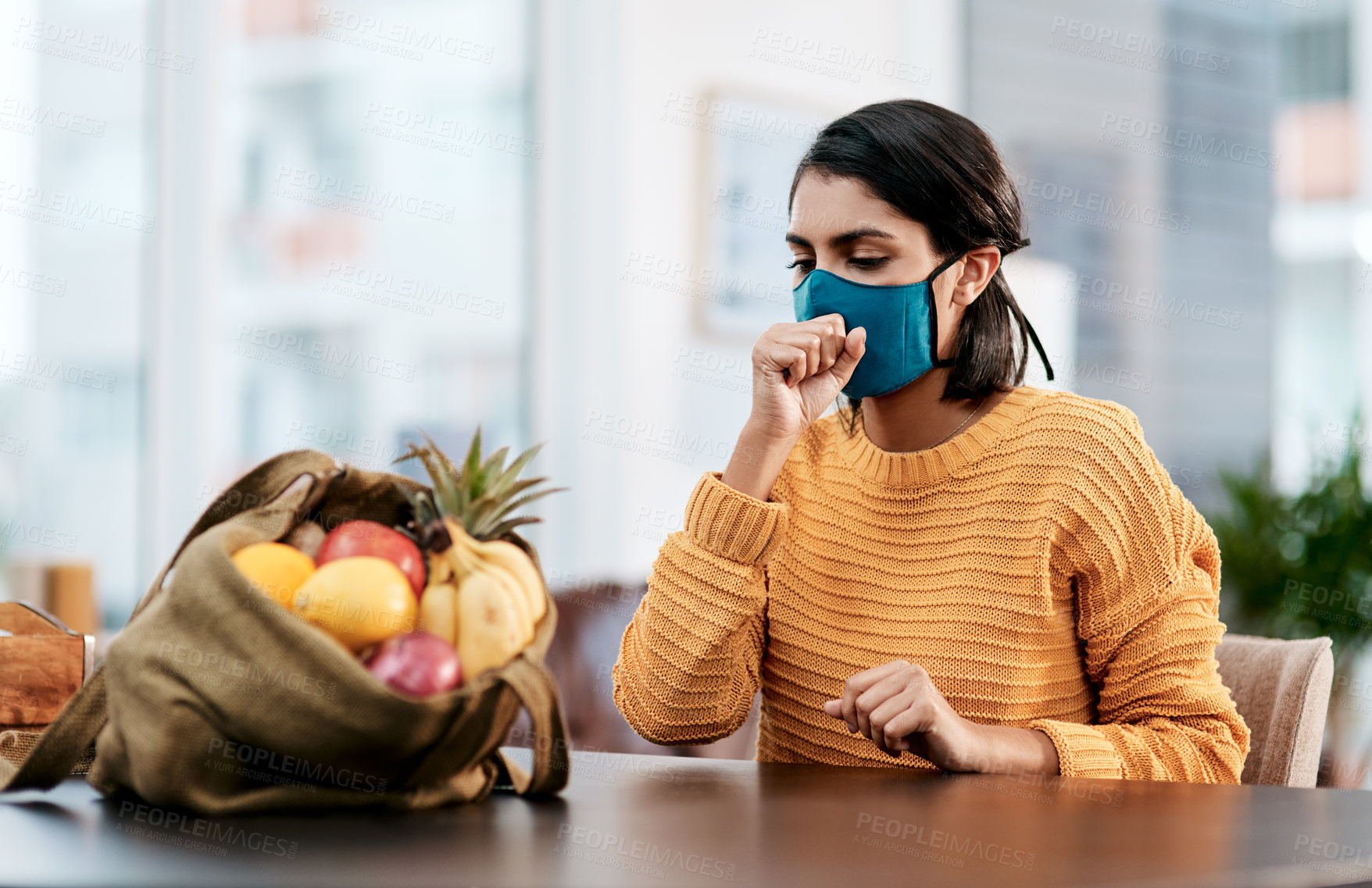 Buy stock photo Shot of a masked young woman coughing after returning home from buying groceries