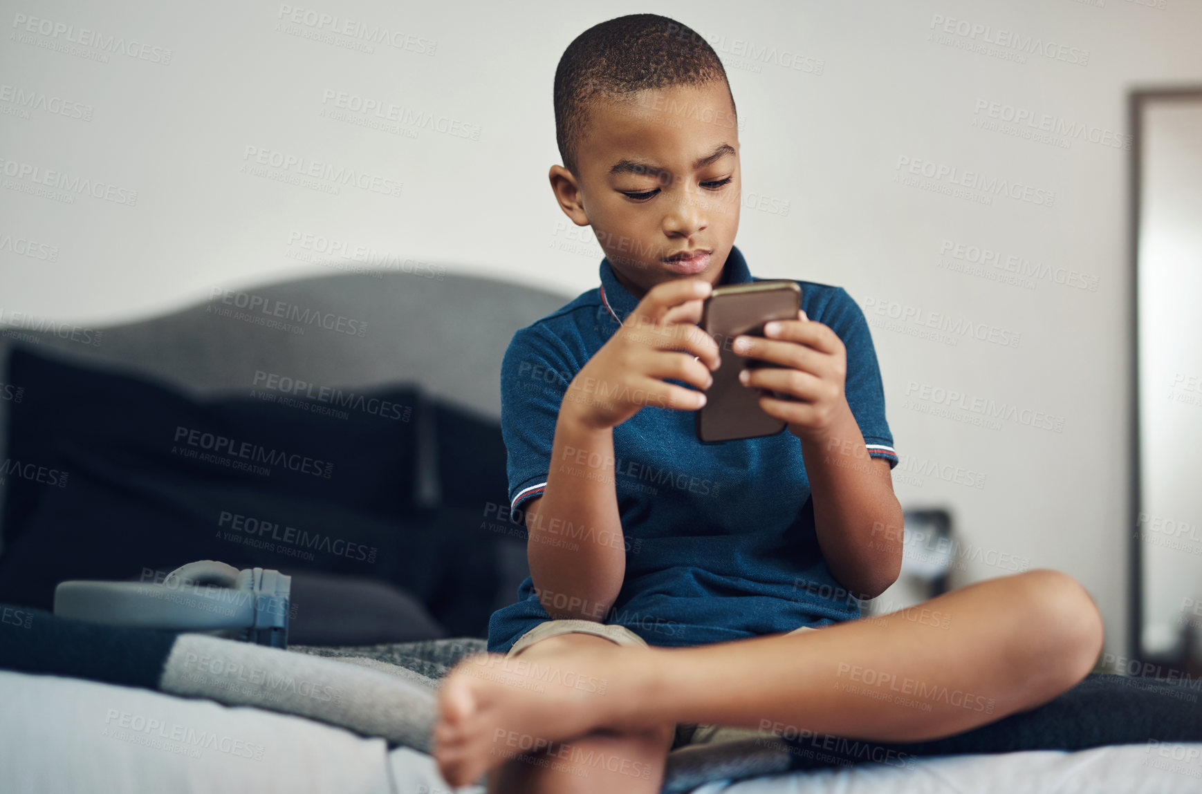 Buy stock photo Shot of a young boy using a cellphone while sitting on his bed