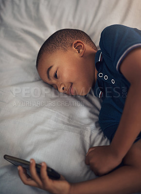 Buy stock photo Shot of a young boy using a cellphone while lying on his bed