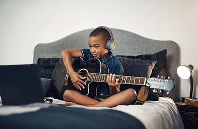 Buy stock photo Shot of a young boy wearing headphones while playing the guitar