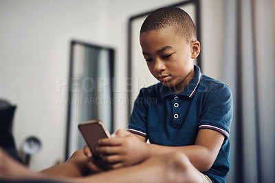 Buy stock photo Shot of a young boy using a cellphone while sitting on his bed