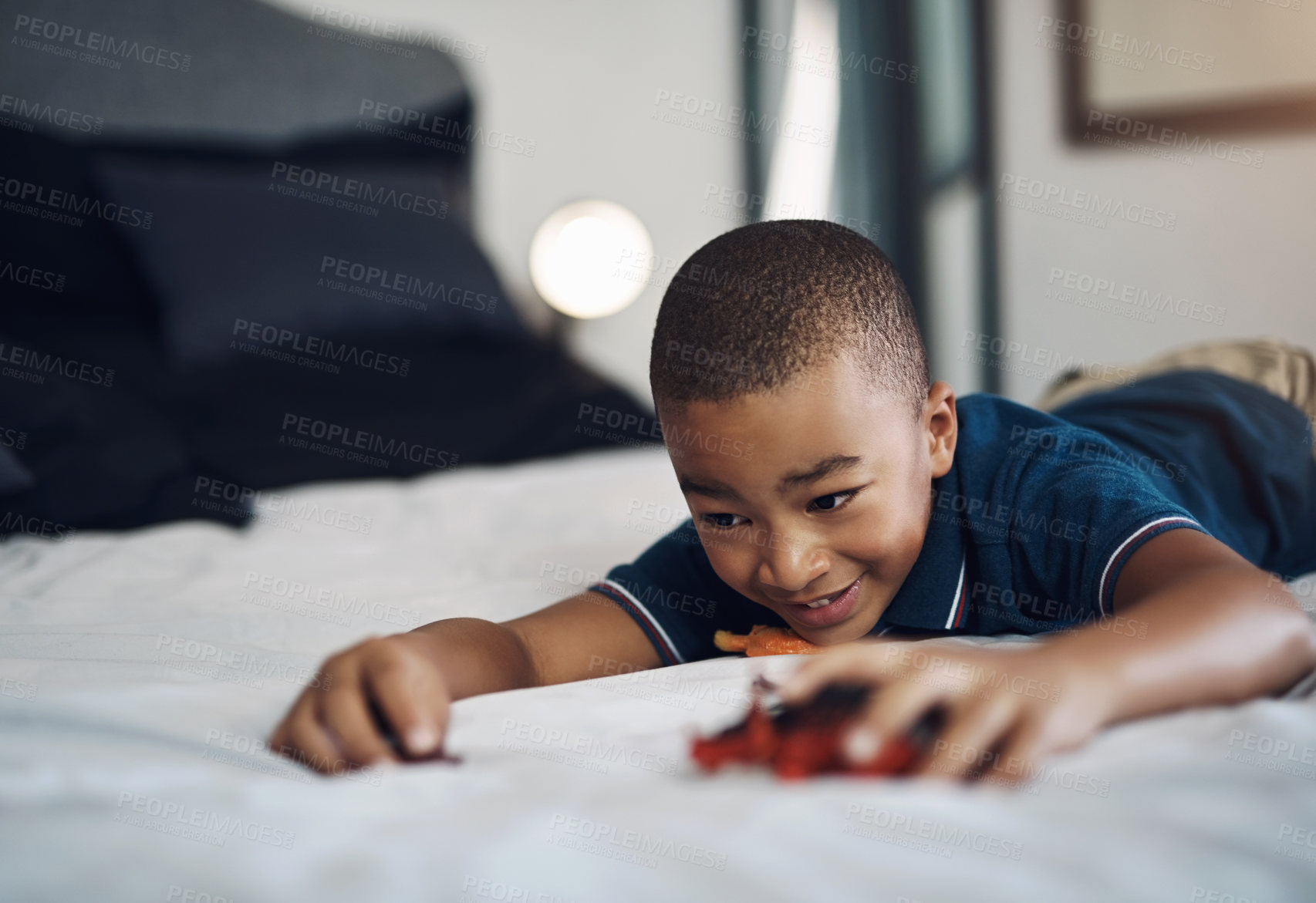 Buy stock photo Cropped shot of an unrecognizable boy playing with dinosaurs while lying on his bed