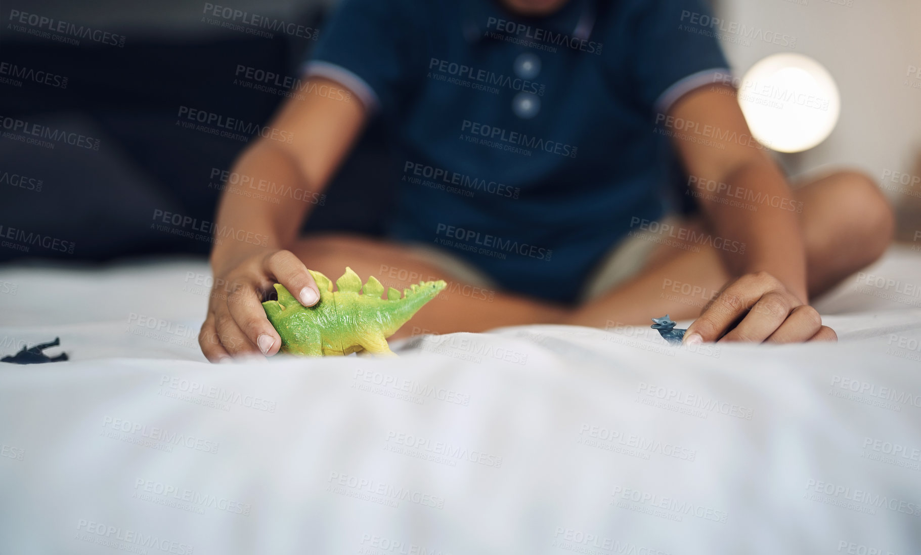 Buy stock photo Cropped shot of an unrecognizable boy playing with dinosaurs while sitting on his bed