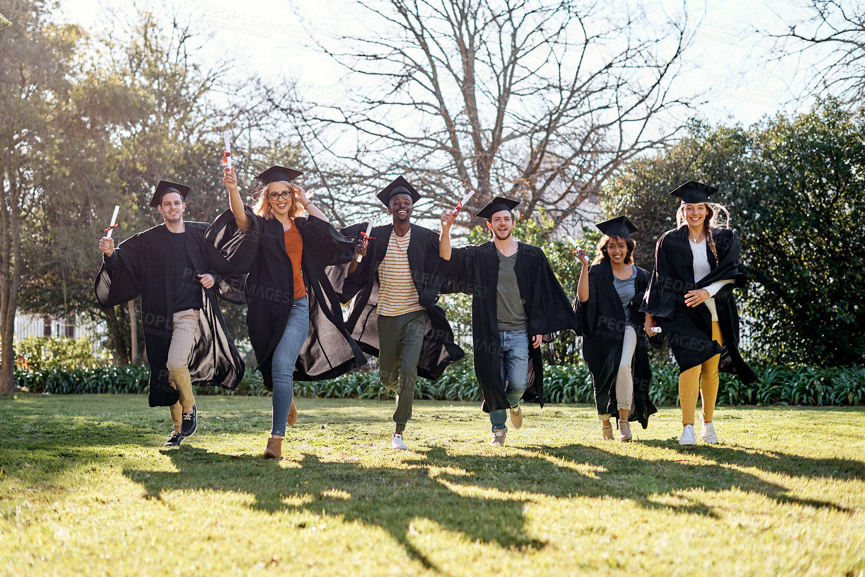 Buy stock photo Portrait of a group of students running together in a row on graduation day