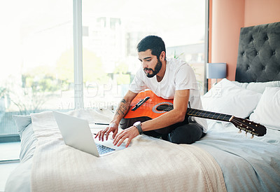 Buy stock photo Shot of a man using his laptop while playing the guitar at home