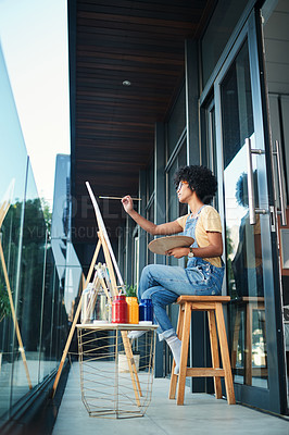 Buy stock photo Shot of a young artist painting on a canvas while sitting on the balcony at home