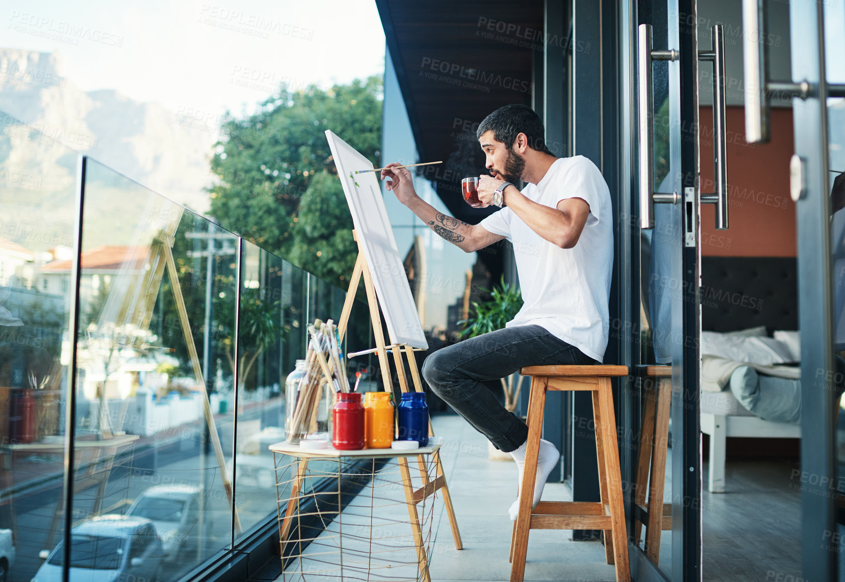 Buy stock photo Shot of a man having tea while doing a painting on the balcony at home