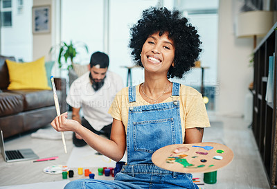 Buy stock photo Shot of a young woman holding a paint palette while her boyfriend sits in the background