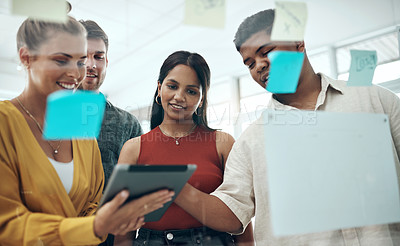 Buy stock photo Shot of a group of businesspeople using a digital tablet while brainstorming with notes on a glass wall in an office