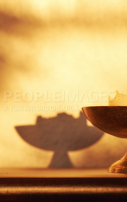 Buy stock photo Closeup of lit candle, a symbol of hope, truth or spiritual in brass holder lighting and illuminating dark home room with copy space. Antique decor on a wooden table for aroma, scent and harmony