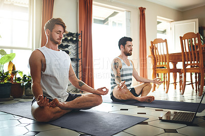 Buy stock photo Shot of two young men using a laptop while meditating in the lotus position at home