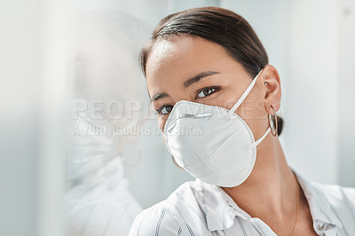 Buy stock photo Shot of a masked young businesswoman leaning against a window in a modern office