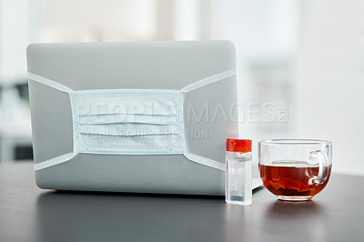 Buy stock photo Shot of a laptop, mask, hand sanitiser and herbal tea on a desk in a modern office