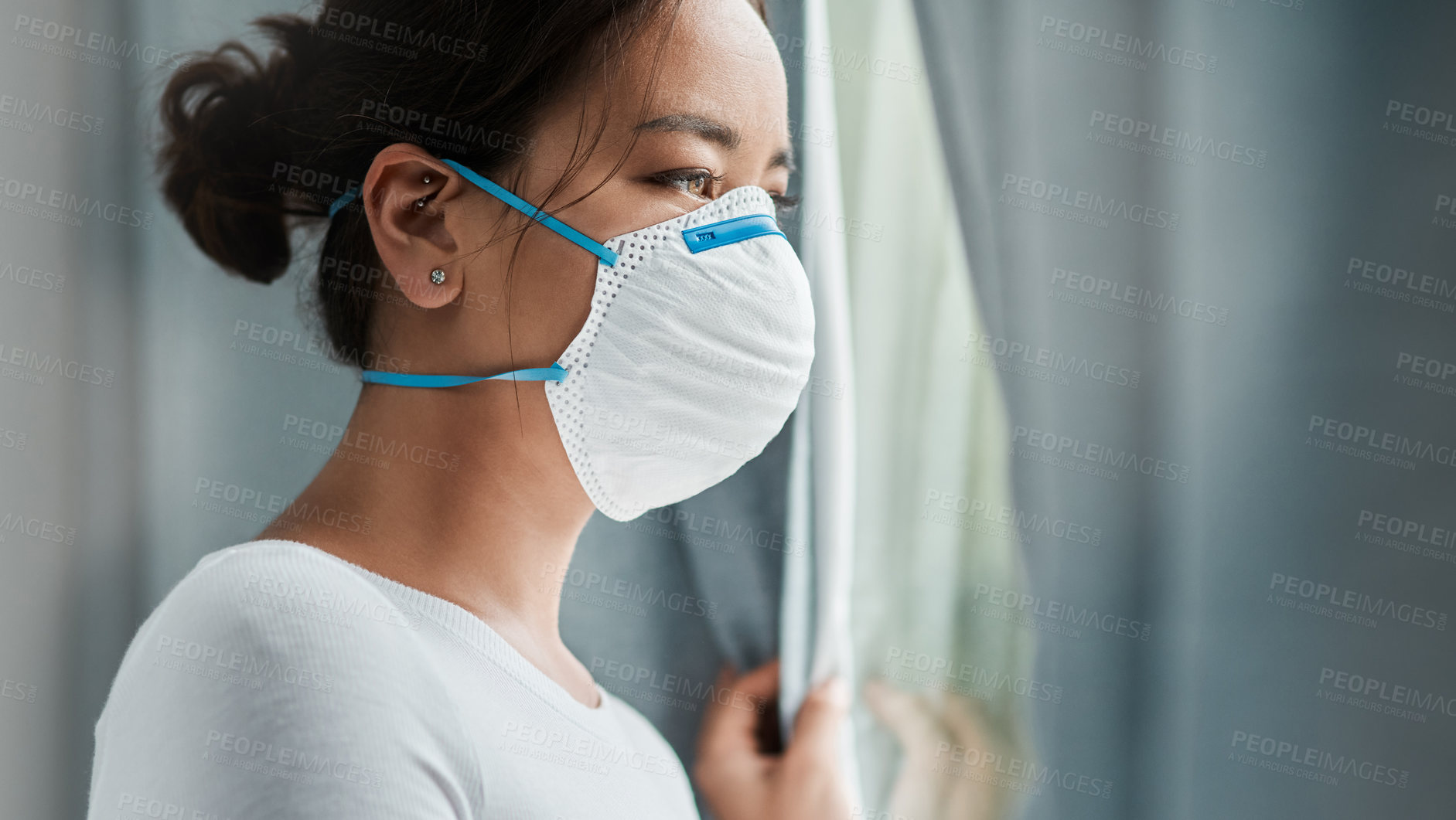 Buy stock photo Shot of a young woman wearing a mask while looking out a window at home