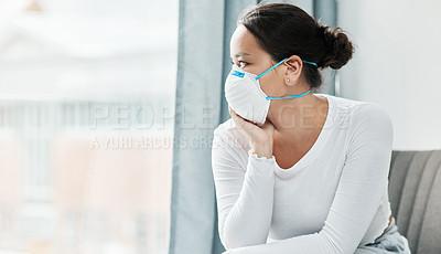 Buy stock photo Shot of a young woman wearing a mask while looking out a window at home