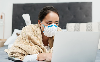 Buy stock photo Shot of a woman wearing a mask while lying on her bed with her laptop