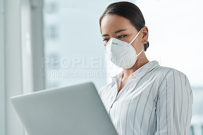 Buy stock photo Shot of a masked young businesswoman using a laptop in a modern office