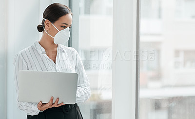 Buy stock photo Shot of a masked young businesswoman holding a laptop and looking out a window in a modern office