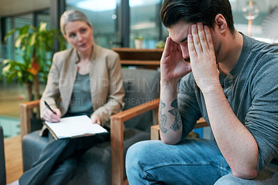 Buy stock photo Shot of a young man having a therapeutic session with a psychologist and looking upset