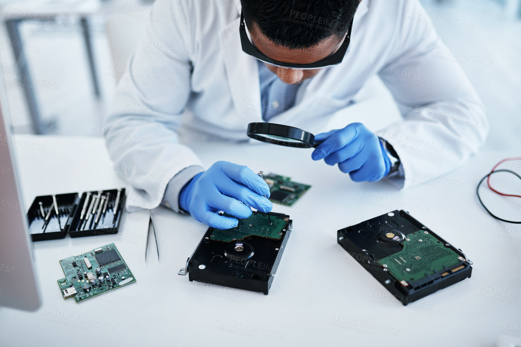 Buy stock photo Shot of a young man using a screwdriver and magnifying glass while repairing computer hardware in a laboratory
