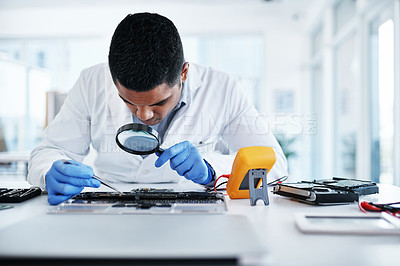 Buy stock photo Shot of a young man using tweezers and a magnifying glass while repairing computer hardware in a laboratory