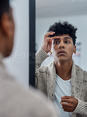 Buy stock photo Shot of a handsome young man inspecting his face in the bathroom mirror