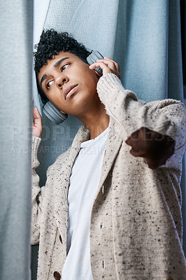 Buy stock photo Shot of a young man using headphones to listen to music while gazing out of the window at home