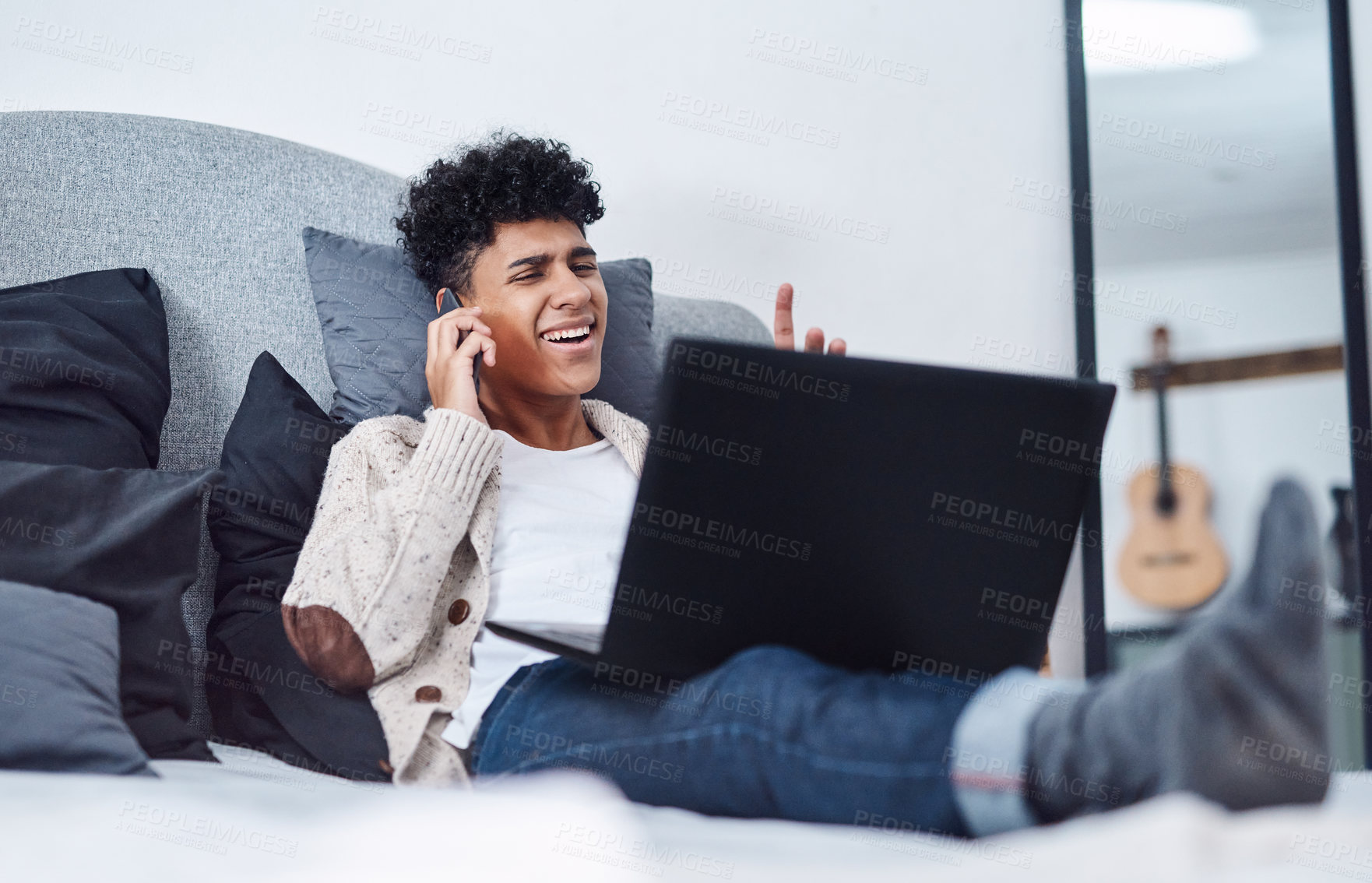 Buy stock photo Shot of a young man using a smartphone and laptop on the bed at home